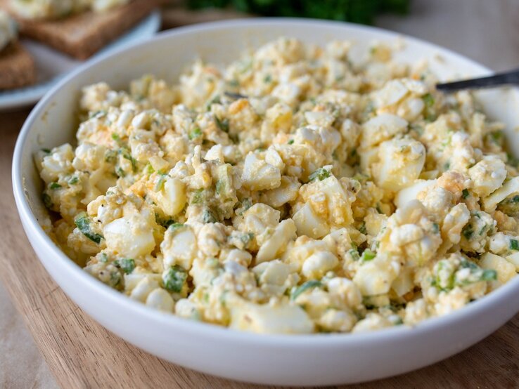 Eiersalat ohne Mayonnaise in runder Porzellanschüssel / Untergrund Holzboden
