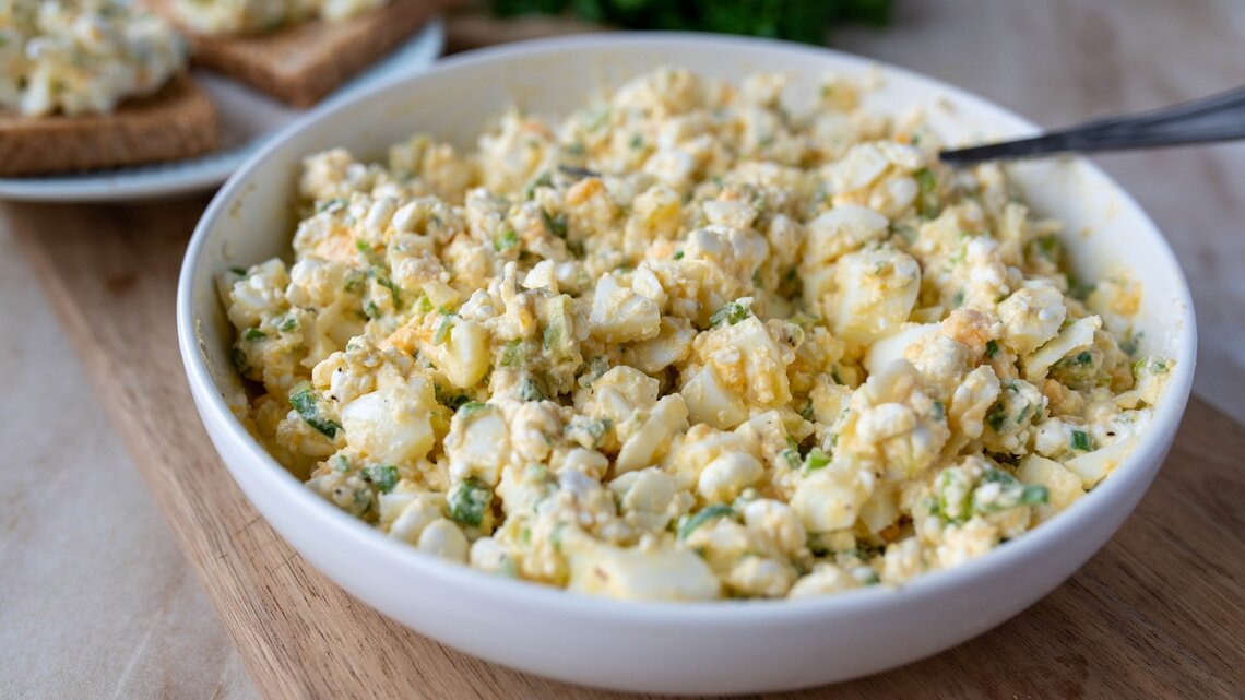 Eiersalat ohne Mayonnaise in runder Porzellanschüssel / Untergrund Holzboden