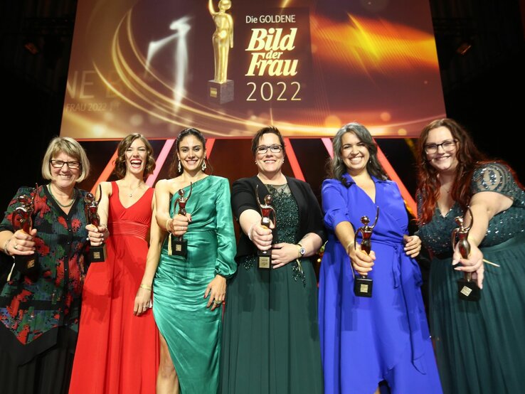 Sechs Preisträgerinnen in Abendkleidern auf der Bühne der GOLDENEN BILD der FRAU-Gala 2022 halten ihre goldene Figurine in die Kamera.